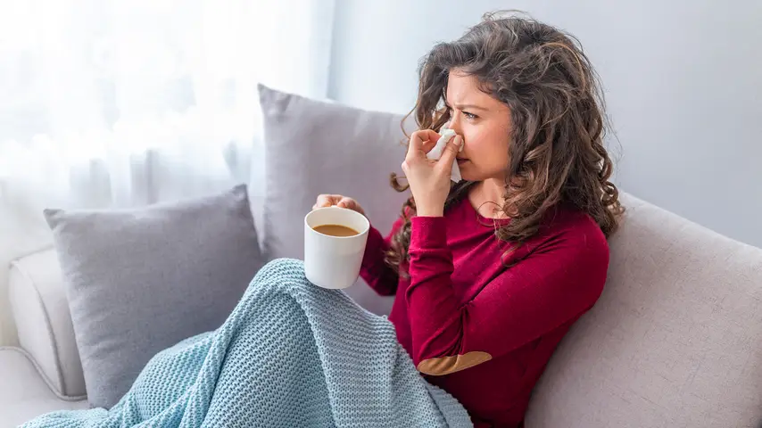 Asian woman has runny and common cold. Cough. Closeup Of Beautiful Young Woman Caught Cold Or Flu Illness. Portrait Of Unhealthy Girl In Scarf Feeling Pain In Throat.